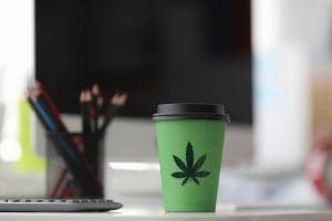 coffe cup wit hcannabis logo on a work desk